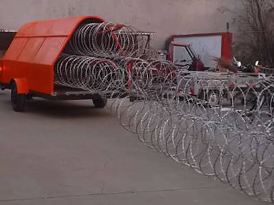 An orange razor wire trailer is stretching concertina razor wire. And the wire has been stretched for a long distance.